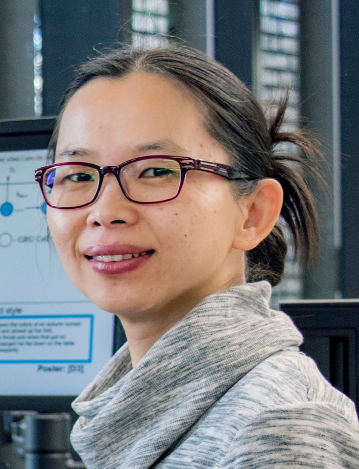 Headshot of Professor Lexing Xie smiling, in the background is a computer screen