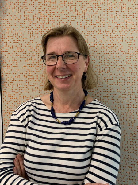 A/P Alice Richardson wears a striped shirt, dark framed glasses, chunky necklace and a smile on her face